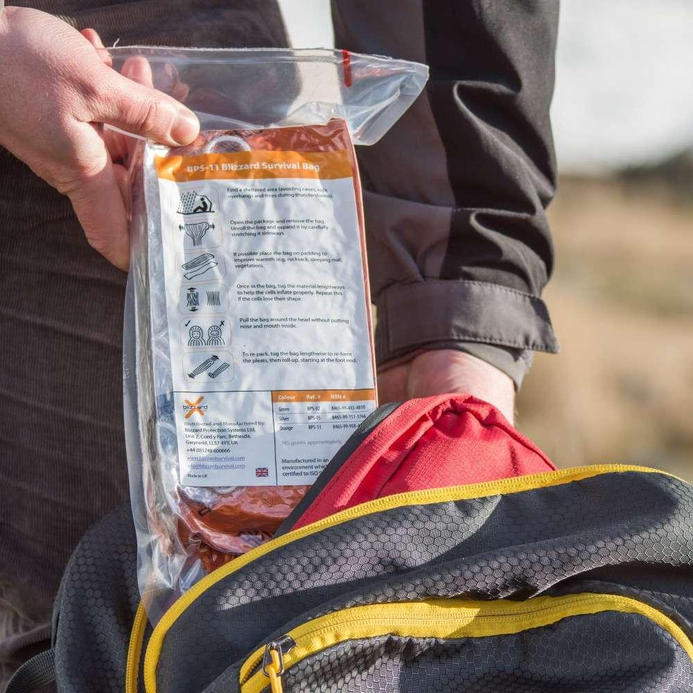 Vacuum-packed Blizzard 3-Layer Survival Bag held in a hand above a rucksack
